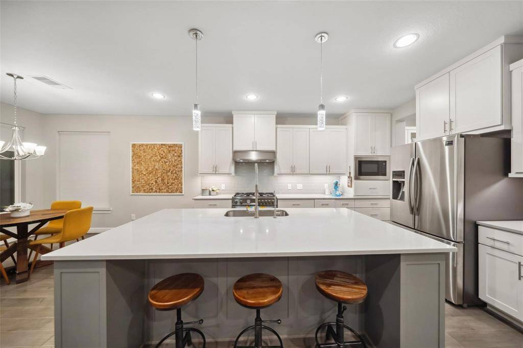 The breakfast bar overlooks a light-filled breakfast nook where an elegant fixture hangs above the perfect spot for morning meals—surrounded by windows that invite the outdoors in.