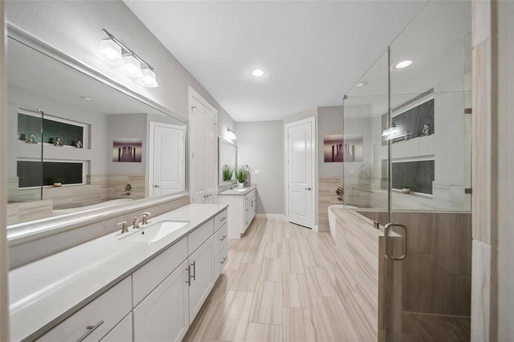 The primary bathroom features elegant wood-look tile flooring, dual sinks, and sleek white cabinetry that provides ample storage—combining style and functionality in a spa-inspired setting.