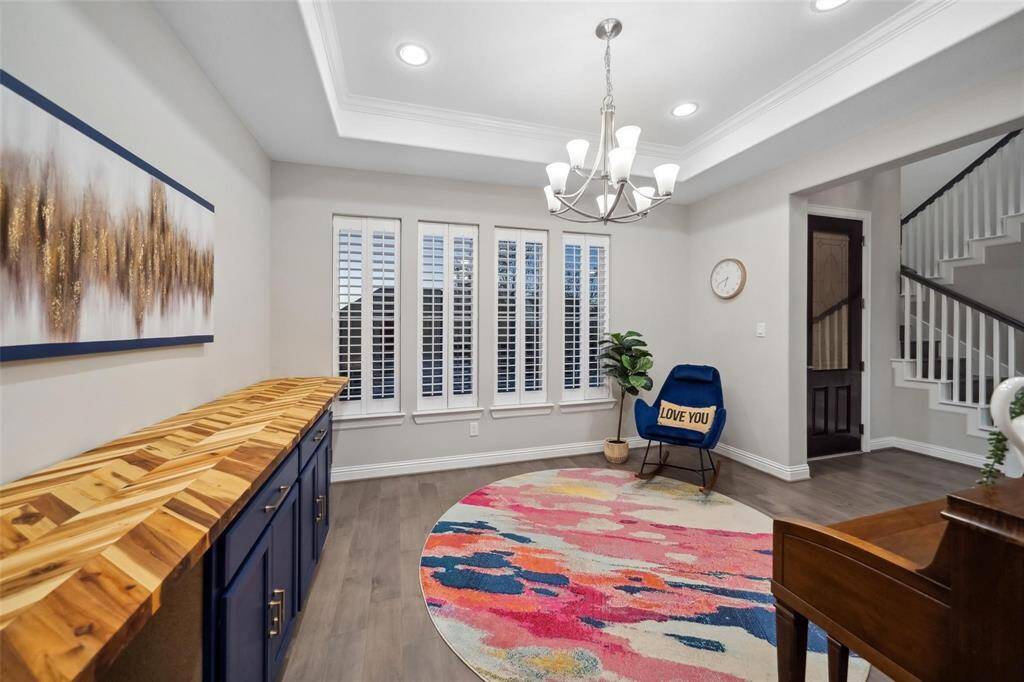 Welcome home—step into the elegant formal dining room, where tray ceilings, a refined chandelier, and a built-in buffet create a timeless setting for gatherings. A wall of windows with shutter-style blinds fills the space with beautiful natural light.