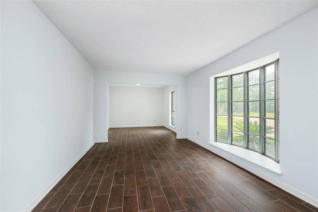 A bay window draws in soft natural light, while dark wood-look tile floors add a rich contrast against crisp white walls—creating a sophisticated space perfect for welcoming guests or relaxing in style in the formal living room.