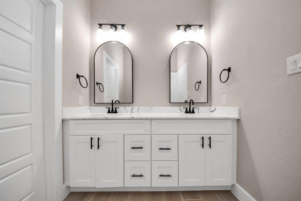 Master Bathroom with modern double vanity with sleek black fixtures, arched mirrors, and elegant lighting. The white cabinets and marble countertop offer a clean, stylish look.