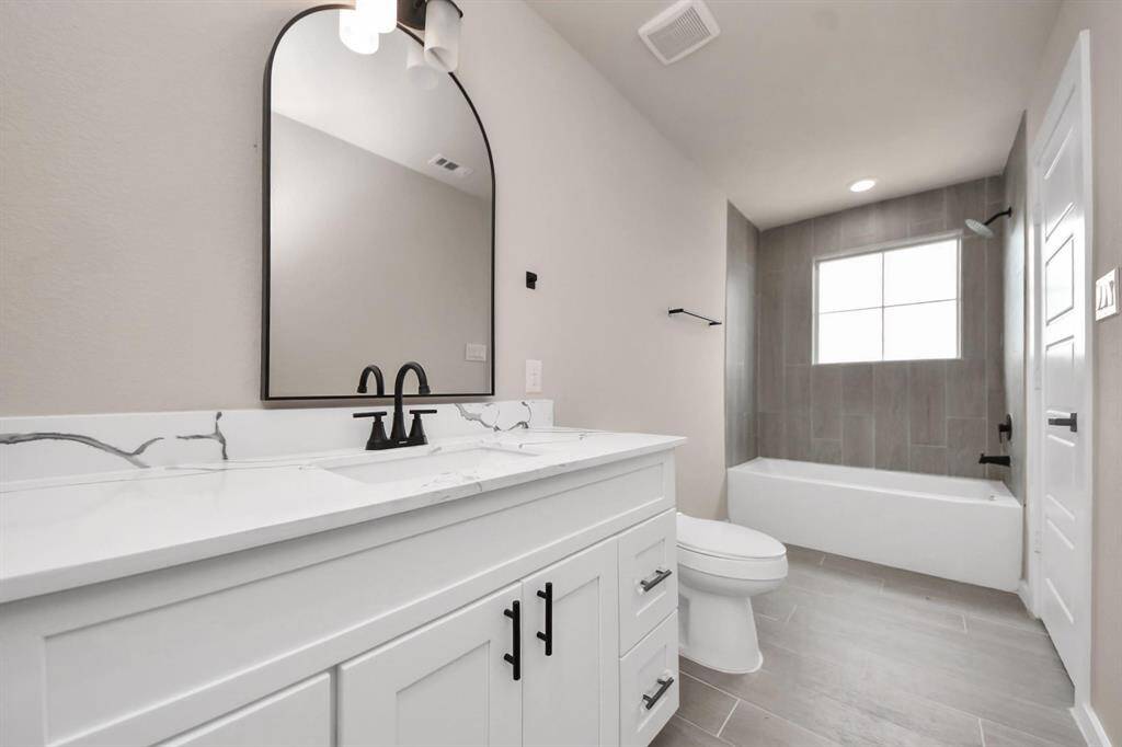 This bathroom features a modern design with a sleek vanity, marble countertop, and stylish black fixtures. It includes a bathtub with a tiled shower area and a large window for natural light.