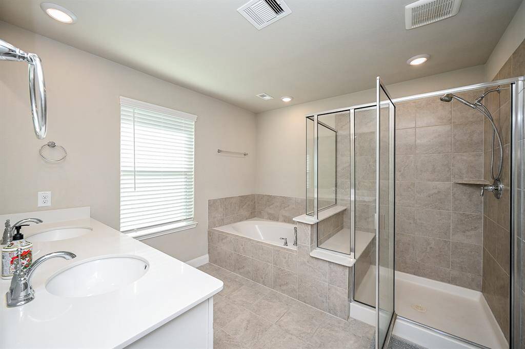 Primary Bathroom with a double vanity, large garden bathtub, and separate glass-enclosed shower. Neutral tiles and ample lighting create a clean, inviting space.