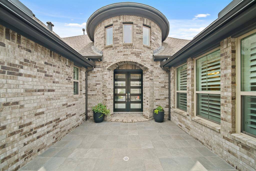 A beautifully designed brick courtyard welcomes you with timeless charm, leading to double glass doors framed by striking curved architectural windows that set the tone for the elegance within.