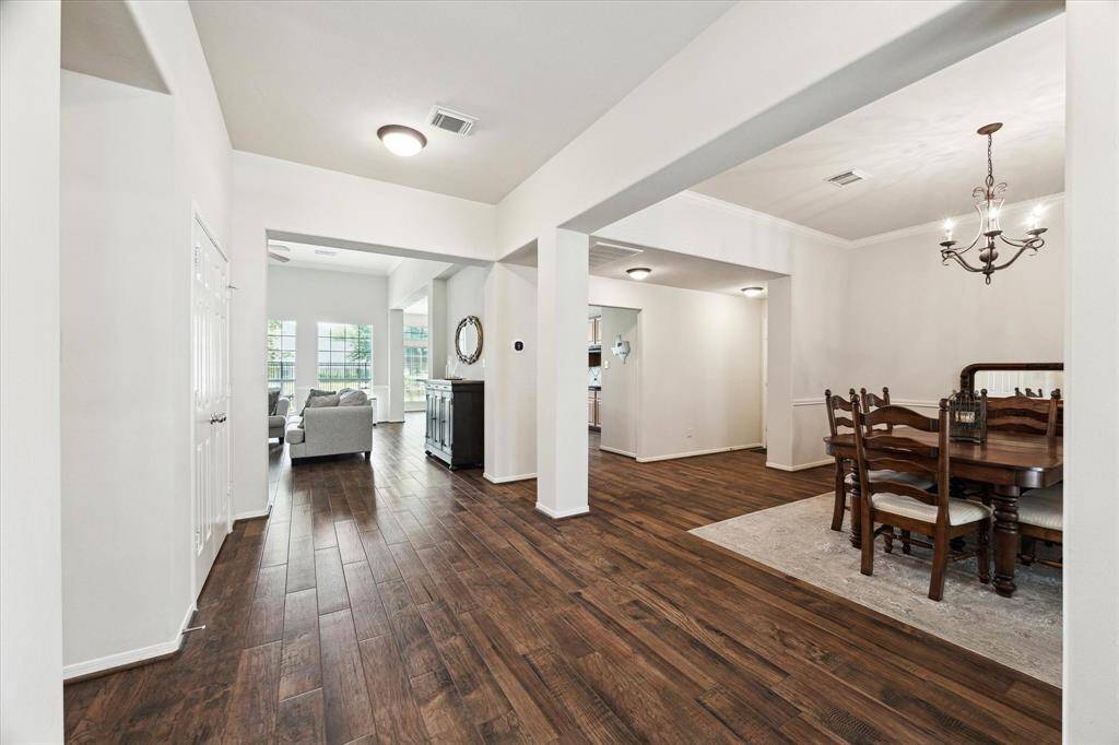 Step into a bright and inviting foyer featuring rich wood-look tile flooring, a fresh neutral color palette, and clear views of the formal dining room to the right, a private study to the left, and the spacious family room straight ahead.