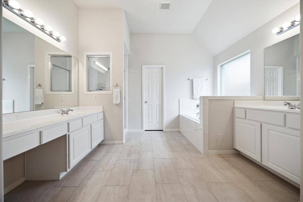 The owner's ensuite bathroom is easy to share with two separate vanities. Each has a full mirror with vanity lights above and one vanity offers knee space to sit while you primp.