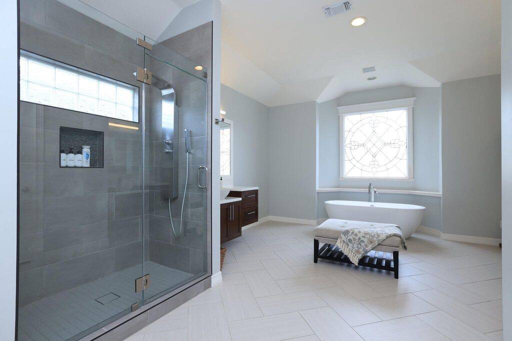 Large walk-in shower with seamless glass enclosre, vanities on opposite sides of the bathroom and a soaking tub centering the room under a leaded glass window.