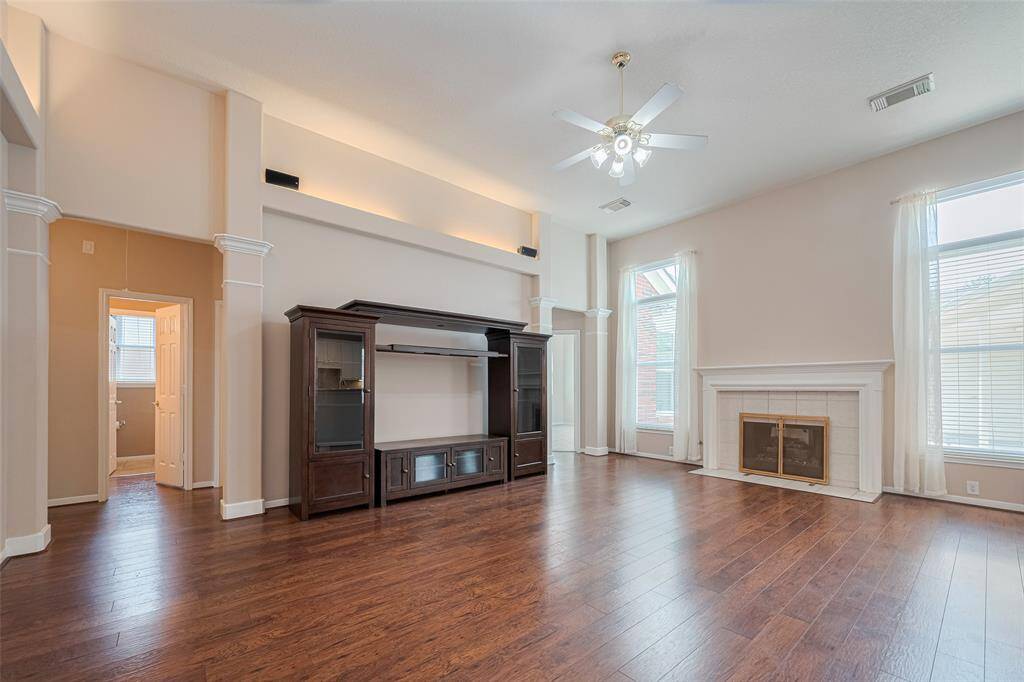 The living room features high ceilings, warm wood-look laminated tile flooring, & up-lighting for added elegance.