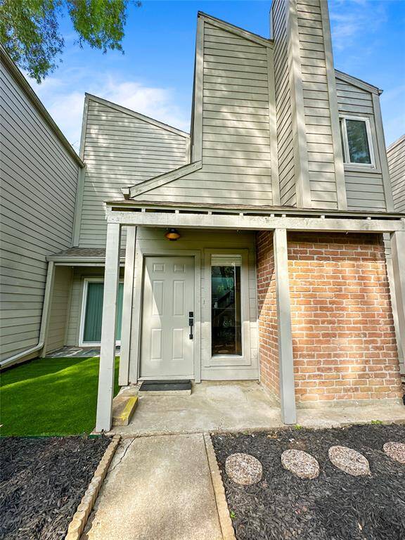 Modern townhouse with a unique architectural design, featuring a mix of brick and siding. The entrance has a covered porch, and there's a small landscaped area with mulch and stepping stones. Ideal for buyers seeking contemporary style.