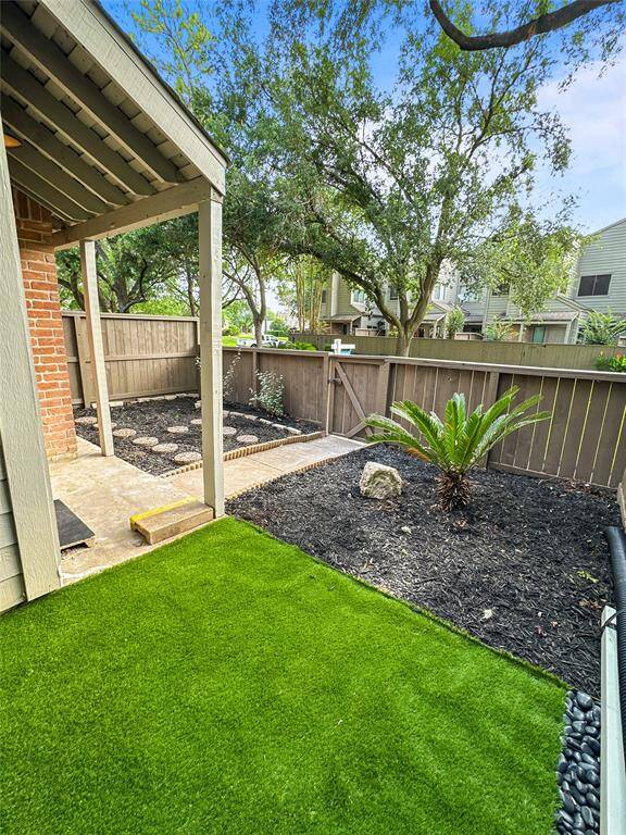 This photo showcases a cozy backyard with a covered patio area, artificial grass, and a small garden bed. The space is enclosed by a wooden fence, offering a private and low-maintenance outdoor area.