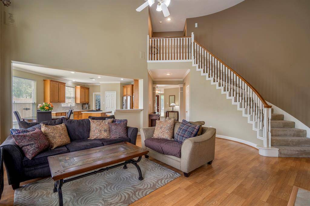Elegant living room with a fireplace, soaring high ceilings, expansive windows, and a grand staircase leading upstairs, creating a dramatic and welcoming entrance.