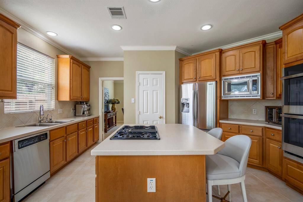 Spacious kitchen with a dining area, large island with seating, abundant natural light from oversized windows, and modern stainless steel appliances.