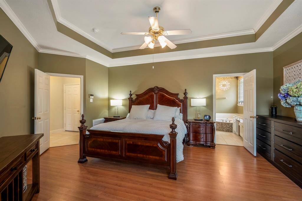 Spacious primary bedroom with crown molding, large windows, a generous seating area, direct patio access, and an en suite bathroom.