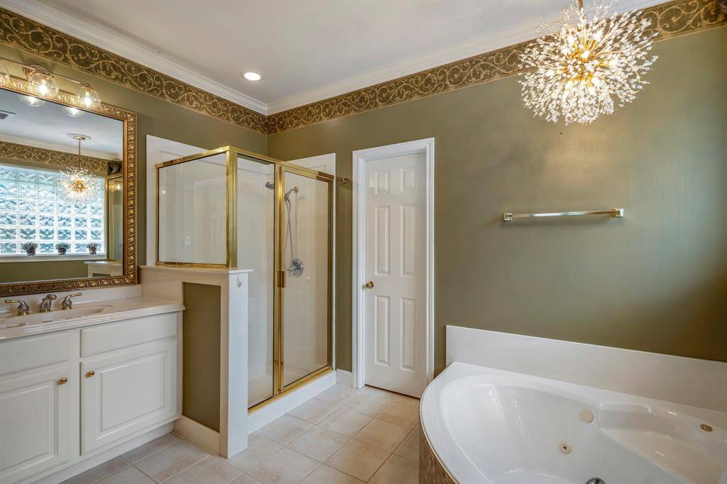Elegant en suite bathroom featuring white cabinetry, a beautiful gold-framed mirror, a stylish chandelier, and a luxurious jetted bathtub.