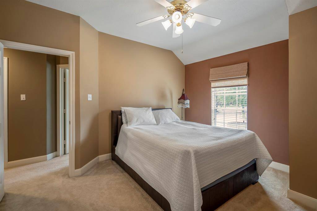 Cozy bedroom with a vaulted ceiling and ceiling fan, featuring a large arched window allowing natural light creating a warm and inviting atmosphere.