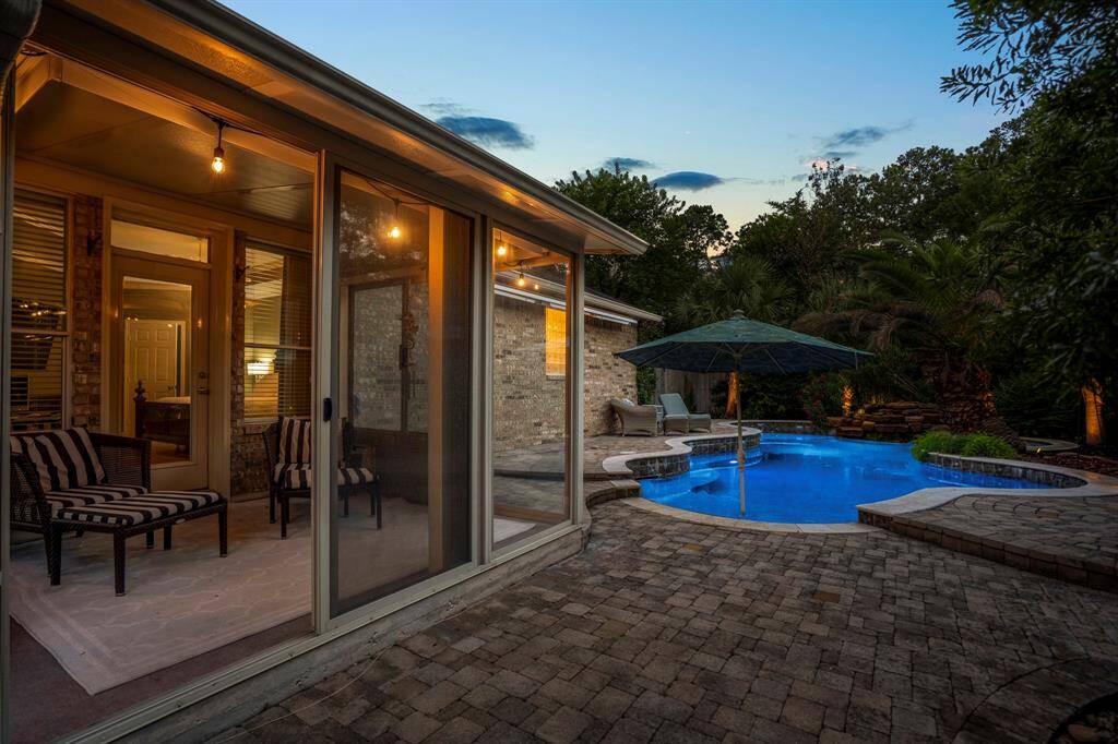 This inviting backyard features a cozy screened patio with seating and a beautifully lit pool surrounded by lush landscaping. Ideal for relaxation and entertaining.