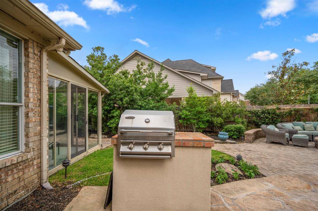 Spacious backyard featuring a built-in grill and a cozy patio with outdoor seating, and lush greenery for privacy. Perfect for entertaining and relaxation.