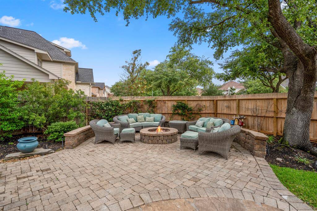 This backyard features a cozy, paved patio with a central fire pit. Mature trees and greenery provide a serene, private atmosphere, ideal for outdoor relaxation and entertaining.