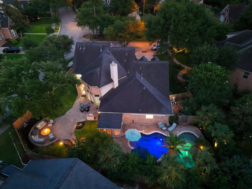 This aerial view showcases the spacious home with a beautifully landscaped backyard featuring a pool and spa area. The outdoor space includes a cozy fire pit with seating, surrounded by lush greenery, perfect for entertaining.