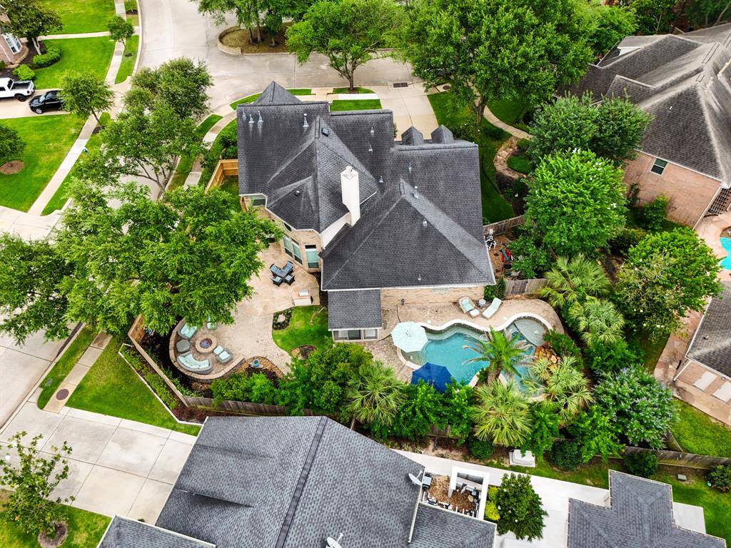 This aerial view showcases a spacious home on a corner lot with a lush backyard, featuring a pool and spa surrounded by mature trees and landscaping. The property offers ample outdoor living space and privacy, ideal for relaxation and entertaining.
