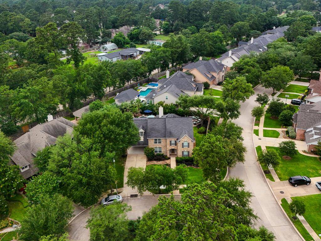 This aerial view showcases a charming suburban neighborhood with tree-lined streets and well-maintained homes. The featured house has a spacious yard and a backyard pool, offering a private oasis. The area is lush with greenery, providing a serene and inviting atmosphere.