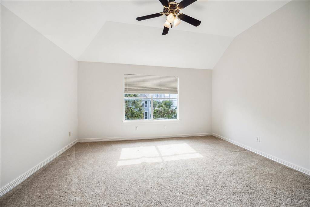 Bright, spacious bedroom with neutral walls, carpet flooring, a ceiling fan, and a large window offering natural light and a view of greenery.