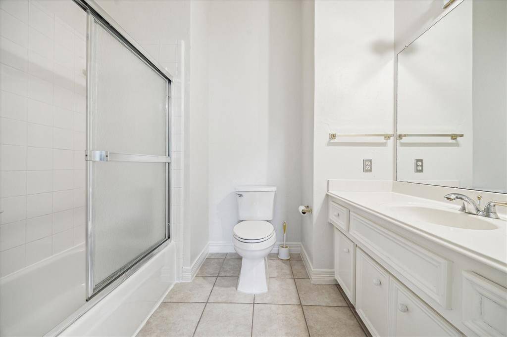 This bright bathroom features a tiled floor, a large vanity with dual sinks, a spacious mirror, and a shower-tub combo with glass sliding doors.