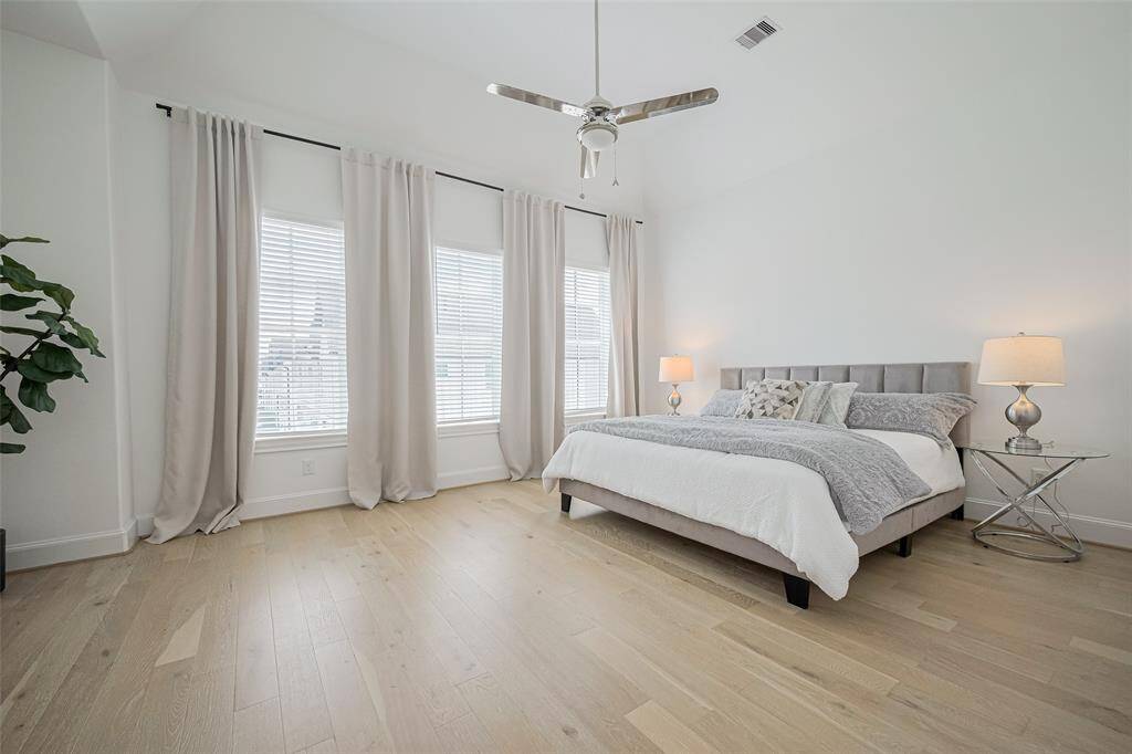 A grand primary bedroom! Tall windows and wood floors help create the simple beauty of this room.