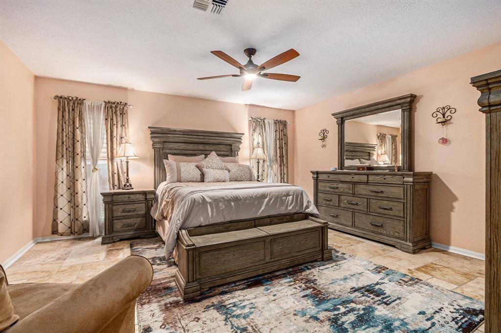 Primary bedroom on the first floor offers the same mixed size Travertine flooring, Roman shades on the two windows, soft paint colors for a relaxing feeling after a long day.