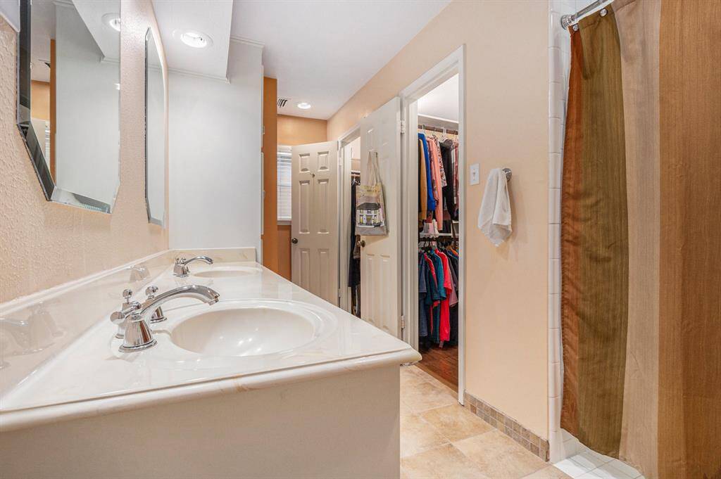 Cultured marble counter and vanity with two sinks, tile flooring and his and her closets.