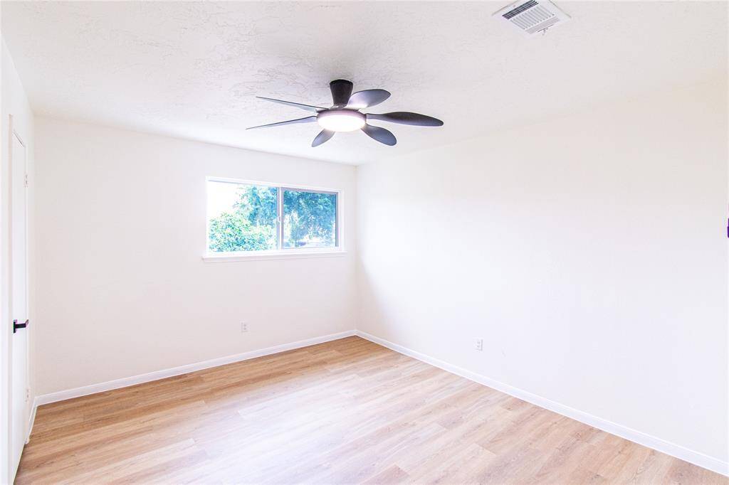 Bright and airy, this bedroom features elegant flooring, a modern ceiling fan, and a large window with serene views. Perfect for comfort and relaxation.