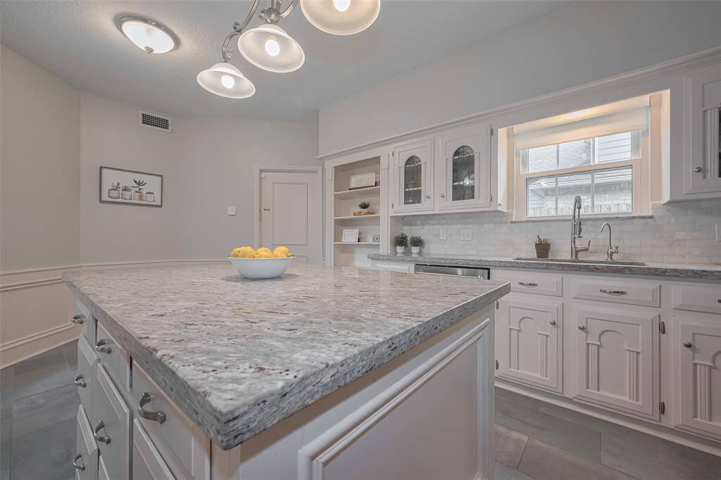 An under-mount sink is perfectly positioned beneath a window with views of the side yard and driveway, bringing in natural light. The dishwasher sits just to the left for added convenience and efficiency in daily routines.