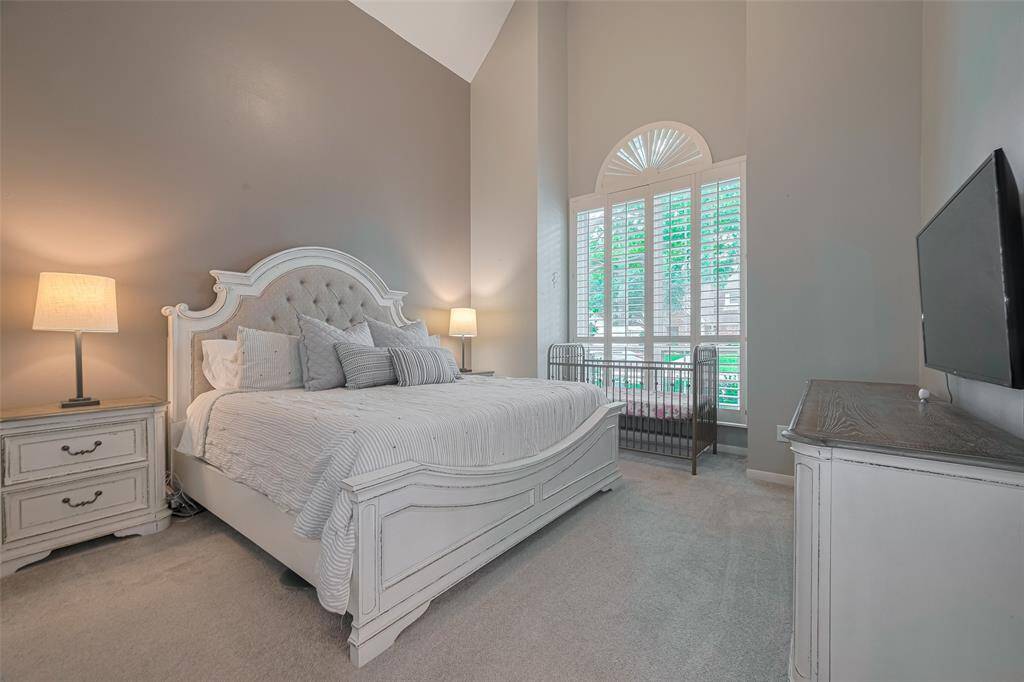 Welcome to your serene primary retreat, featuring a vaulted ceiling, soft decorator paint tones, plush carpeting, and a large window with plantation shutters that filters in natural light while offering privacy and charm.