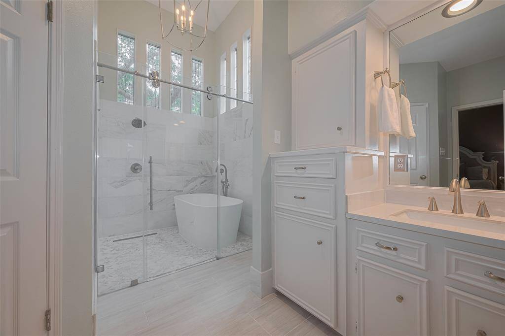 Welcome to your spa-like ensuite bathroom (remodeled in 2024), showcasing crisp white cabinetry, dual vanities with sleek countertops, and a beautifully remodeled walk-in shower. A luxurious freestanding tub completes the space, perfect for unwinding at the end of the day.