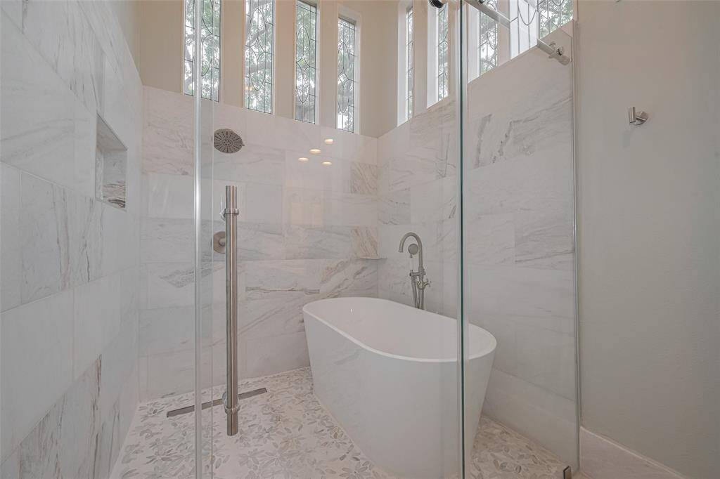 The custom walk-in shower showcases a neutral tile surround and a freestanding tub within, all accented by polished nickel hardware. Stunning leaded glass windows bathe the space in natural light while maintaining privacy—creating a serene, spa-inspired atmosphere.