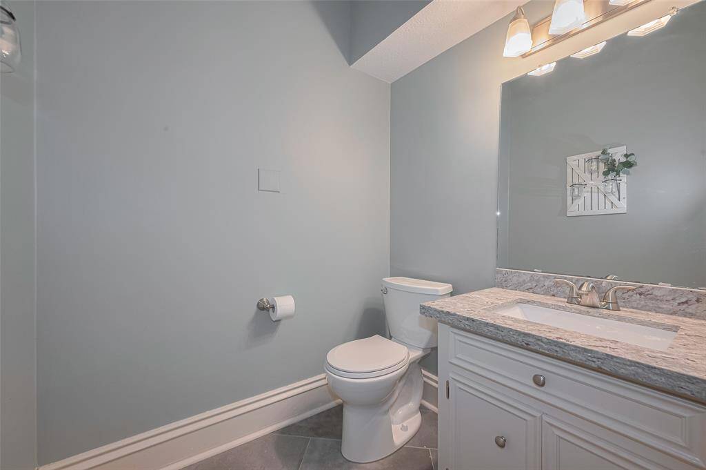 The spacious powder bath features updated tile flooring, rich decorator paint, and thick baseboards for a polished finish. A stylish vanity with gorgeous countertops adds a touch of sophistication to this thoughtfully designed space.