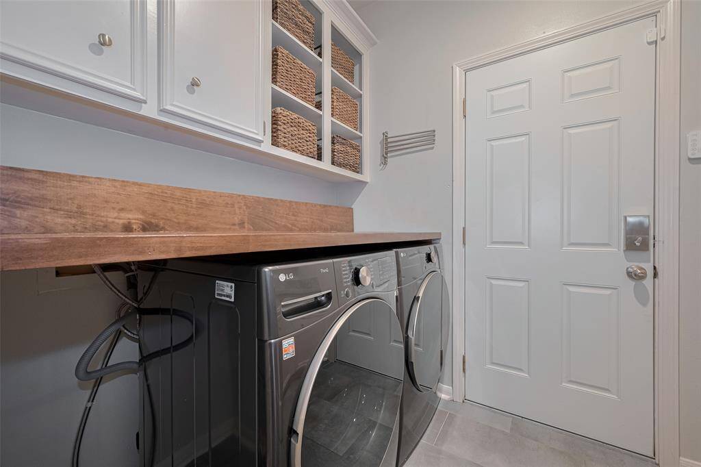 The utility room is thoughtfully designed with built-in cabinetry, including open-faced sections ideal for baskets and organized storage. A built-in shelf with hanging space adds convenience for laundry and daily tasks.