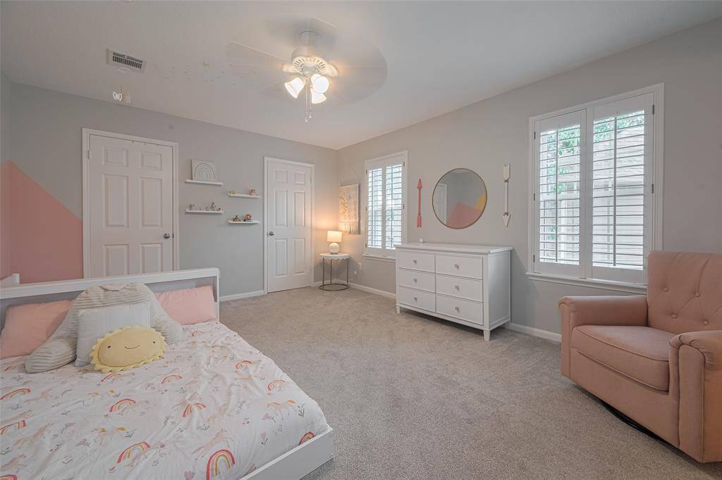 Guest bedroom two is generously sized, featuring plush carpeting, soft decorator paint, and a ceiling fan for comfort. Two large windows with plantation shutters fill the room with natural light.