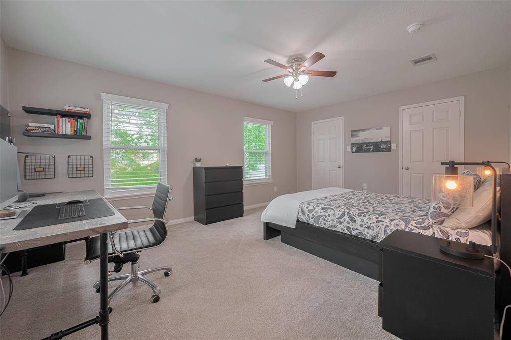 Guest bedroom three features plush carpeting, a ceiling fan, and soothing decorator paint. Two large windows flood the room with natural light, creating a bright and welcoming atmosphere.