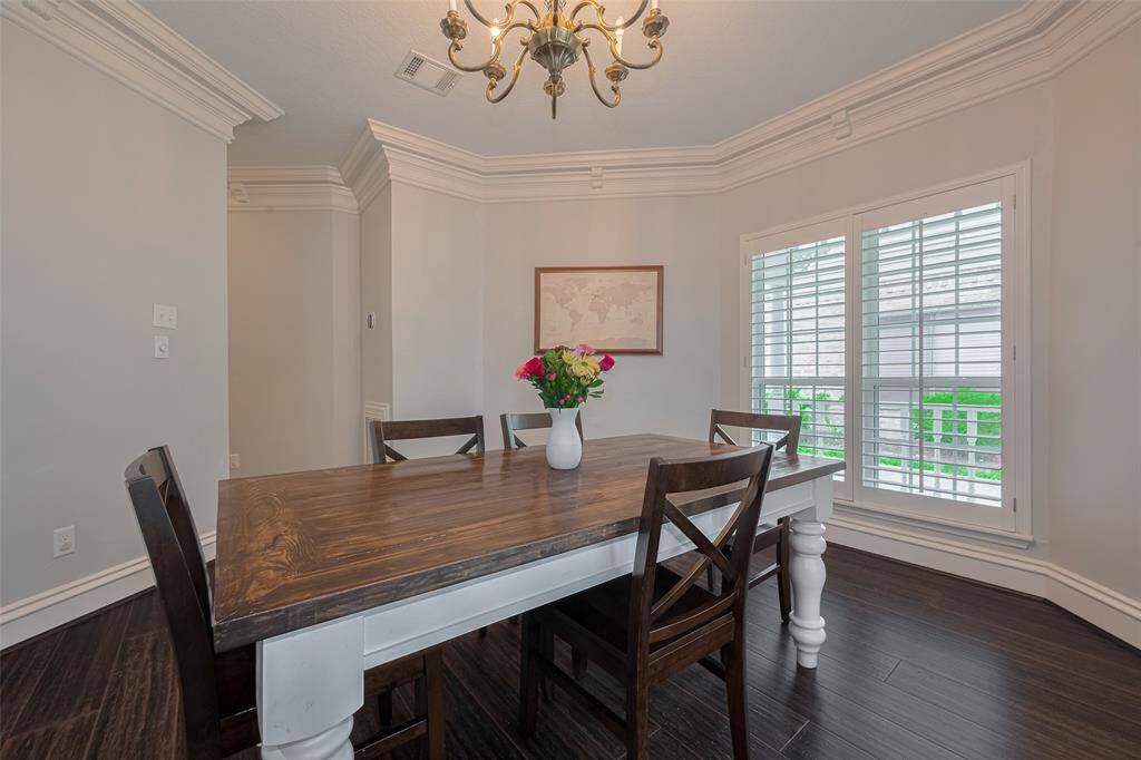 Just off the entry, the elegant dining room features rich wood flooring, double crown molding with intricate detailing, and decorator paint. A large window with classic plantation shutters offers a lovely view of the front porch, filling the space with natural light and timeless charm.