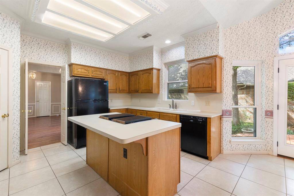 This spacious kitchen features a center island with cooktop, classic wood cabinetry, and abundant natural light, offering functionality and charm with seamless access to the backyard.