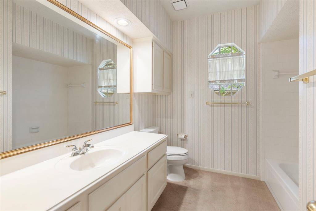 The full secondary bath features a large vanity, soaking tub with shower, and charming natural light through a decorative window.