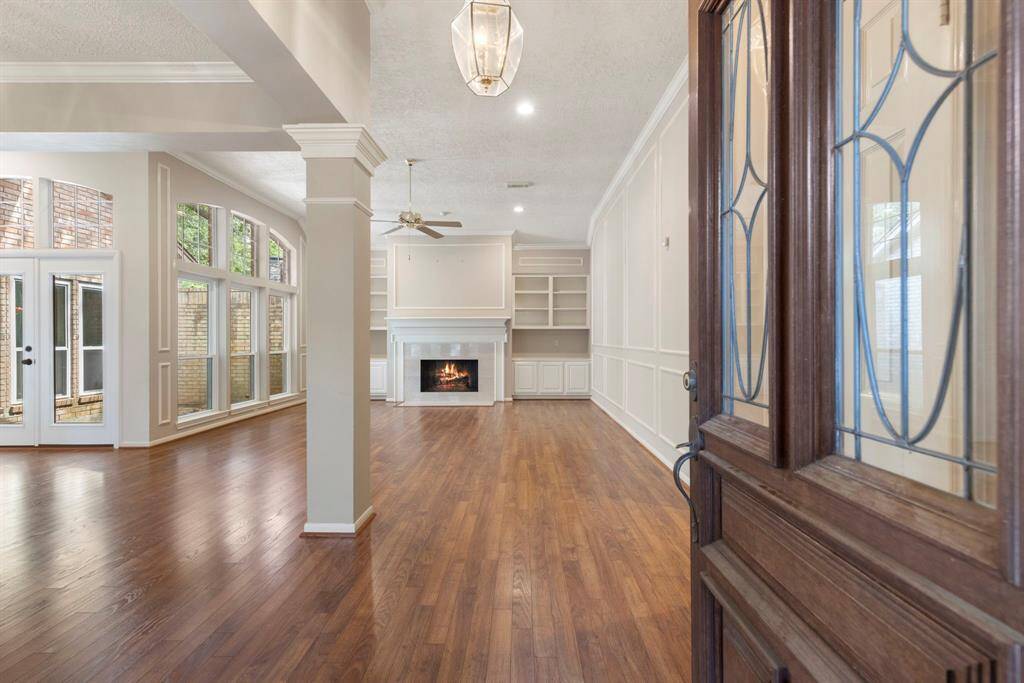 Step inside to a light-filled living space with soaring windows, crown molding, laminate wood floors, and a cozy fireplace framed by custom built-ins.