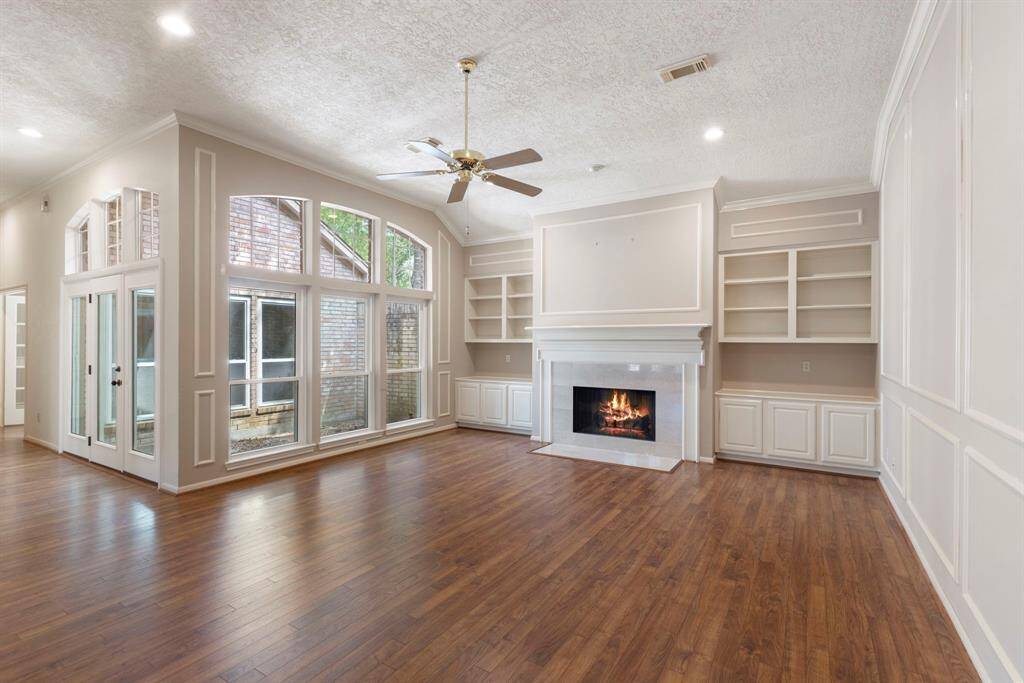 The spacious living room features custom built-ins, recessed lighting, and large windows that frame serene views of the central atrium, bringing the outdoors in.