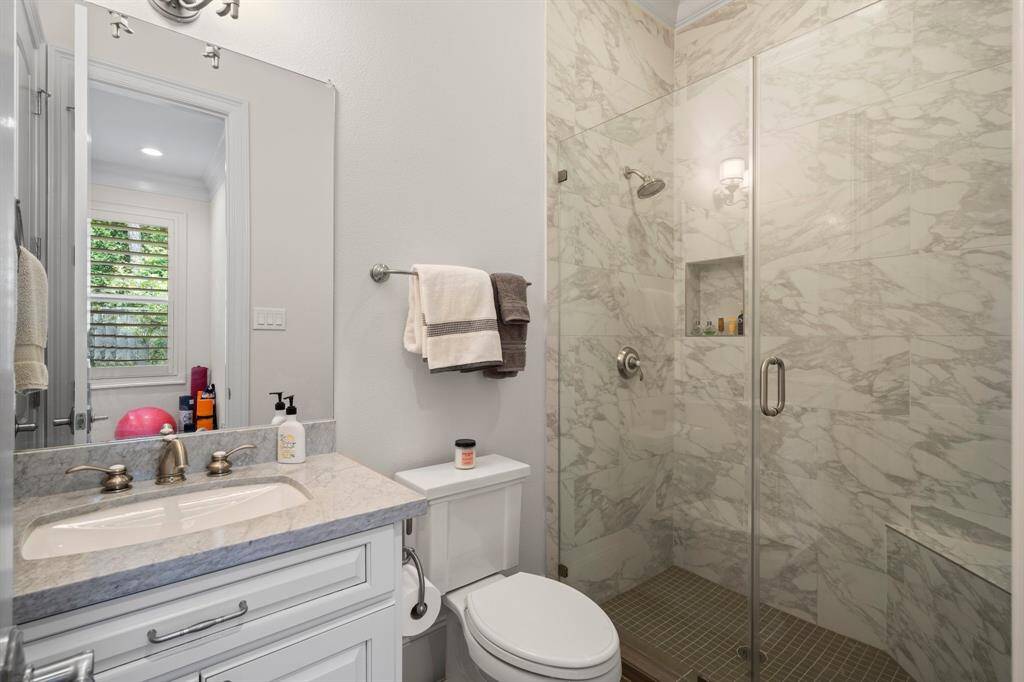 The second full bath on the first floor for guests features wood-look tile flooring, crown molding, single undermount sink with marble countertop, toilet, and tiled shower with corner seat and built-in toiletry niche.