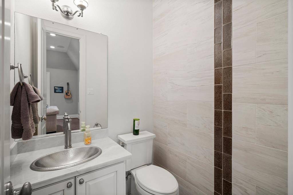 This guest half bath for second floor occupants features tile flooring, crown molding, an artisan-style hammered metal sink with marble countertop, decorative wall tile accents, and toilet.