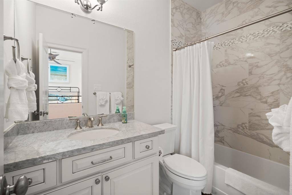 This is just one of three en-suite baths upstairs. This bathroom features rectangular tile flooring, single undermount sink with extended marble counter top, hall linen closet, toilet, and a tiled shower/tub combo with toiletry shelf and decorative tile insets.
