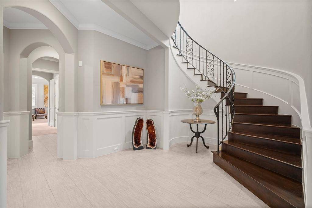 Step into sophisticated style with this stunning two-story foyer, where elegant upgrades like triple crown molding, 9’ baseboards, wainscotting, and the gorgeous curved staircase add to the refined craftsmanship throughout. The grand Foyer welcomes you with warm rectangular tile flooring, two elegant chandeliers, convenient coat closet, and several areas for artwork, an entry table, or bench.