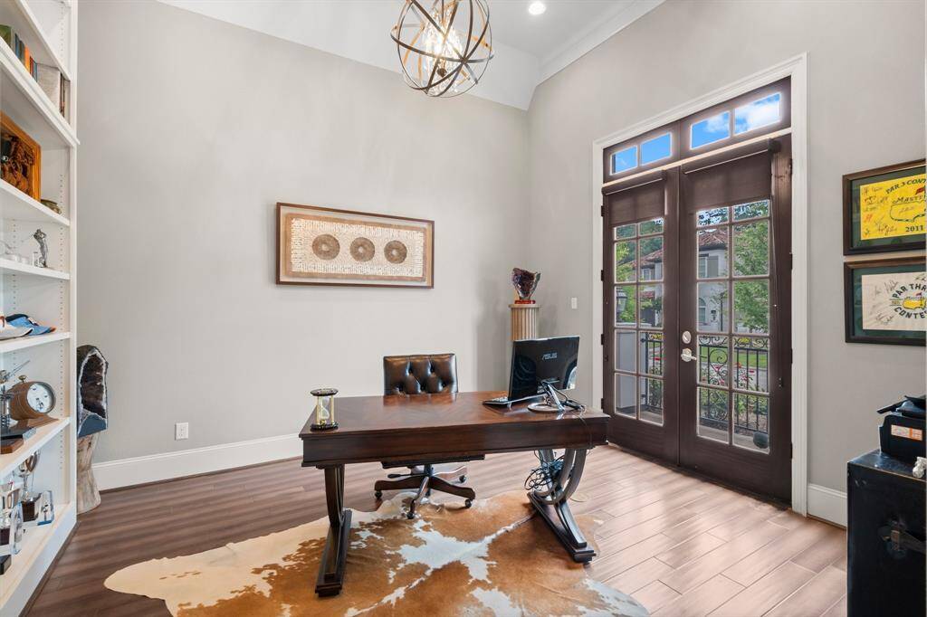 This executive office is a true standout, filled with natural light from two large French doors with transom windows above. These doors lead to a private front patio, where you can sit and sip your morning coffee among the blooming rose bushes before starting work. Elegant wood-look tile flooring, triple crown molding, 9” baseboards, recessed lighting, and an elegant chandelier add a touch of sophistication and comfort."