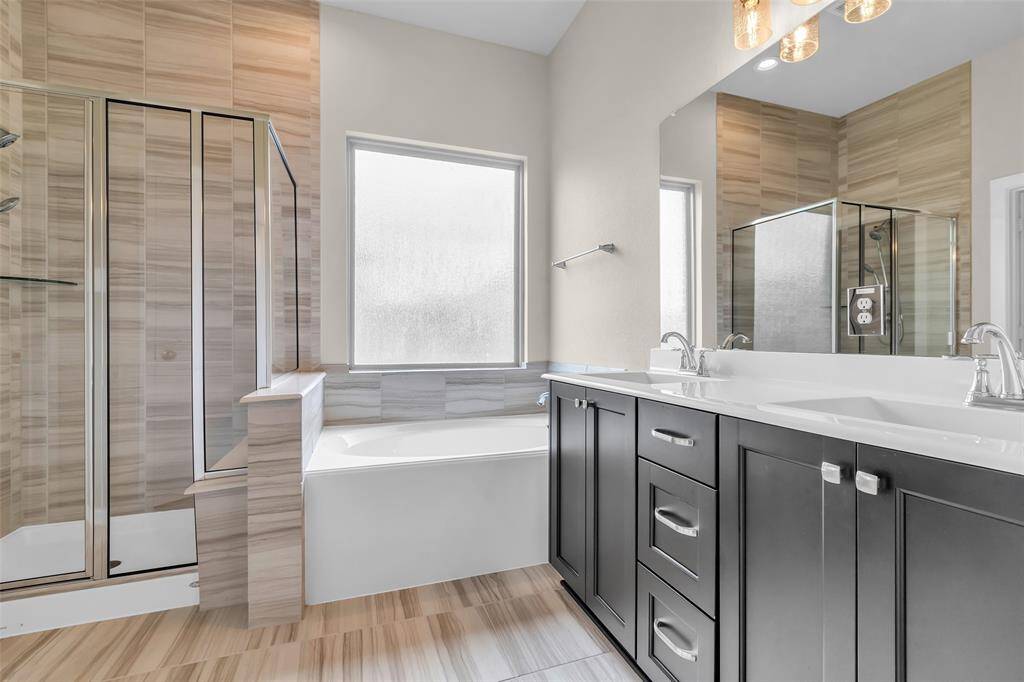 The primary bathroom features double sinks, a separate glass-enclosed shower, a soaking tub, and a large vanity mirror, providing both space and functionality.